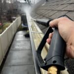 Close-up of gutter cleaning with pressure washer, outdoors, during the day.